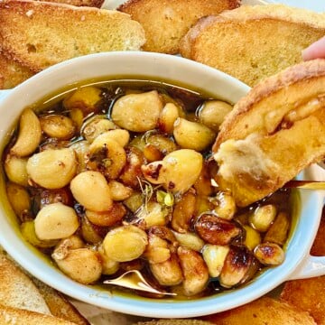 Rustic appetizer of garlic confit in baking dish with toasted baguette