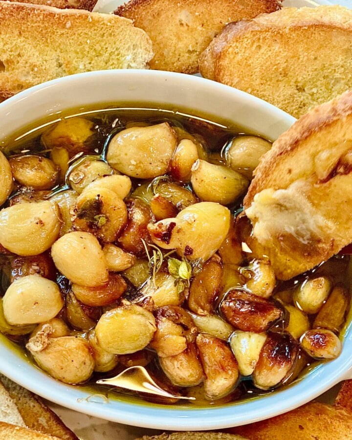 Rustic appetizer of garlic confit in baking dish with toasted baguette
