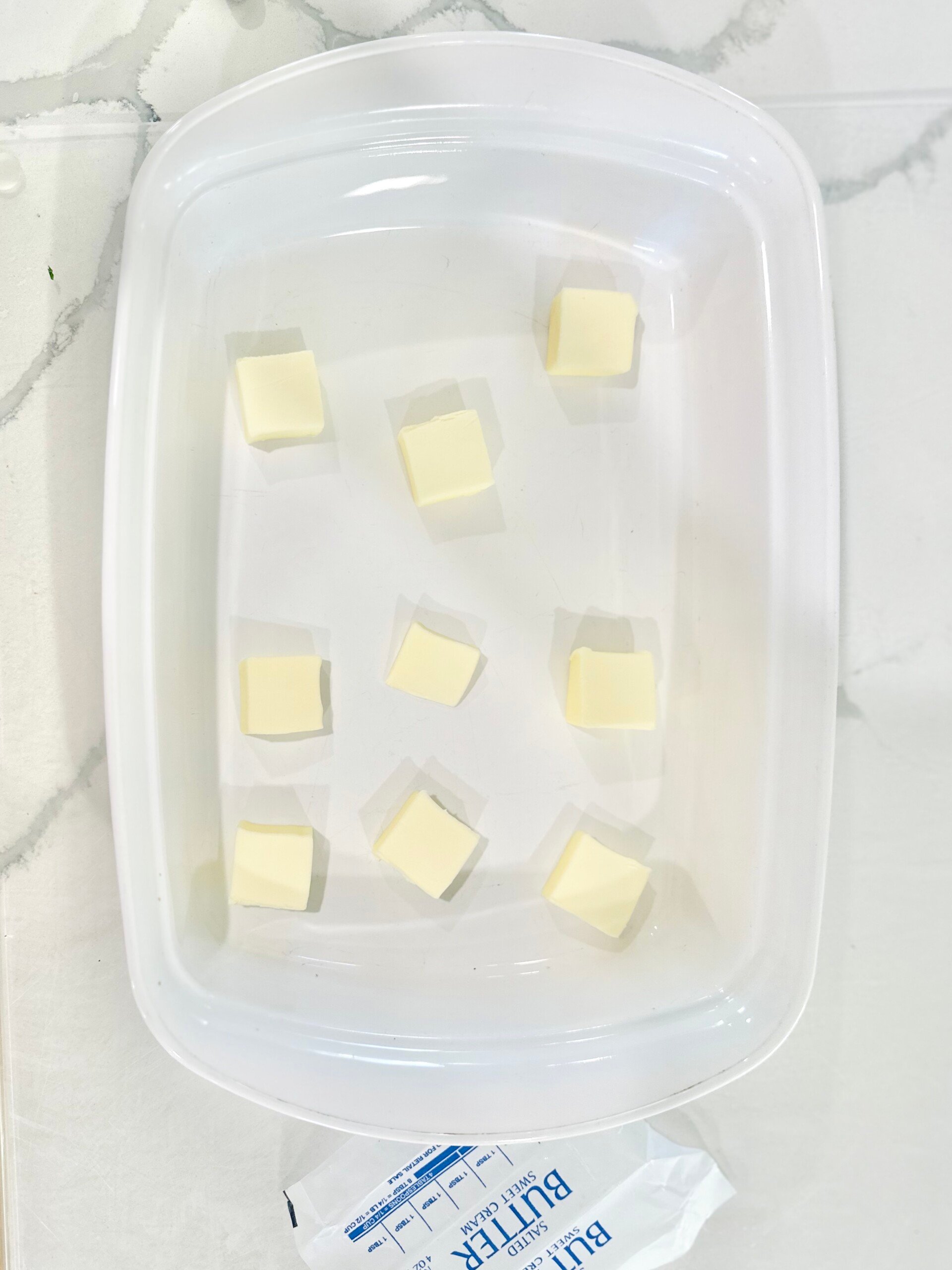 Cubed butter in a white baking dish on marble counter, ready to melt in the oven for pecan pie cobbler base.