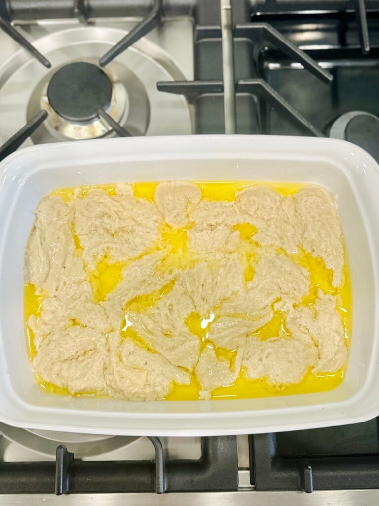 Cobbler batter spooned over melted butter in a white baking dish before adding toppings.