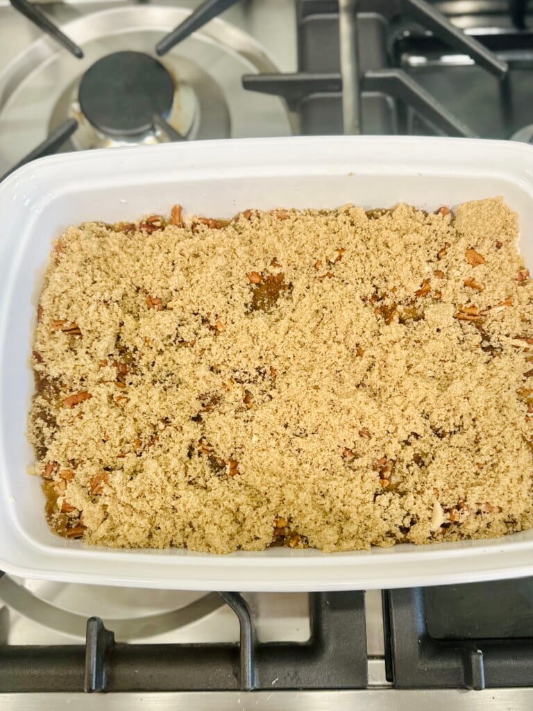 Brown sugar layer spread evenly over pecans in white baking dish for pecan pie cobbler.