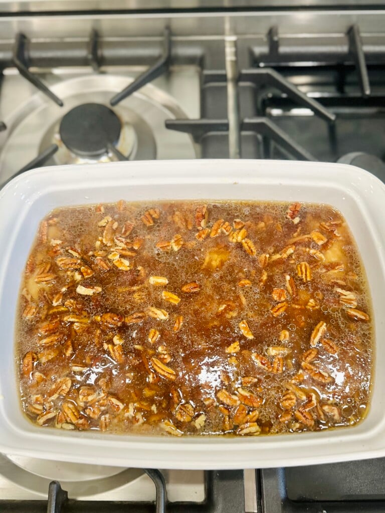 Unbaked pecan pie cobbler in white dish showing pecan topping floating in syrup mixture.