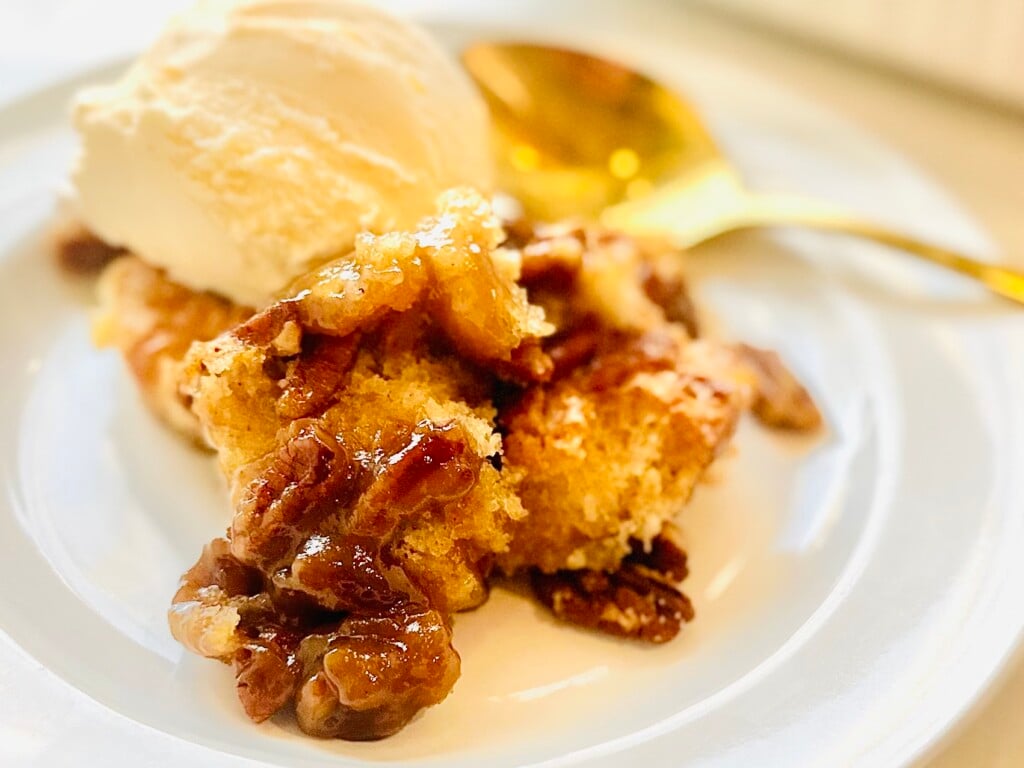 Fully baked pecan pie cobbler with crisp golden top and gooey pecan filling visible in white baking dish.