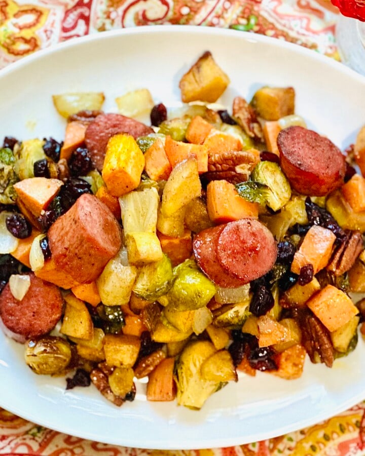 Sheet pan sausage dinner served on a white platter over a colorful fall tablecloth with orange flowers in the background.