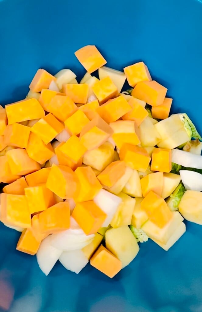 Sliced smoked sausage added to a bowl of chopped sweet potatoes, apples, onions, and Brussels sprouts before seasoning.