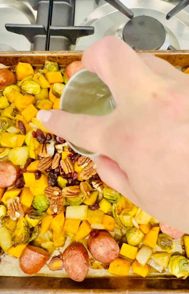 Lemon juice being drizzled over roasted sausage, Brussels sprouts, sweet potatoes, and pecans on the baking sheet.