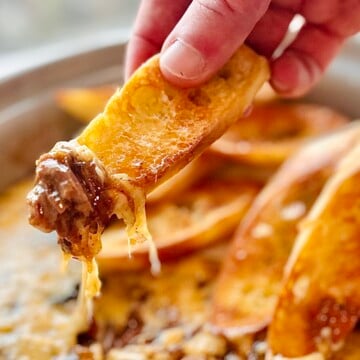Baguette slice lifted from the pot showing tender beef strands and melted Gruyère stretching.
