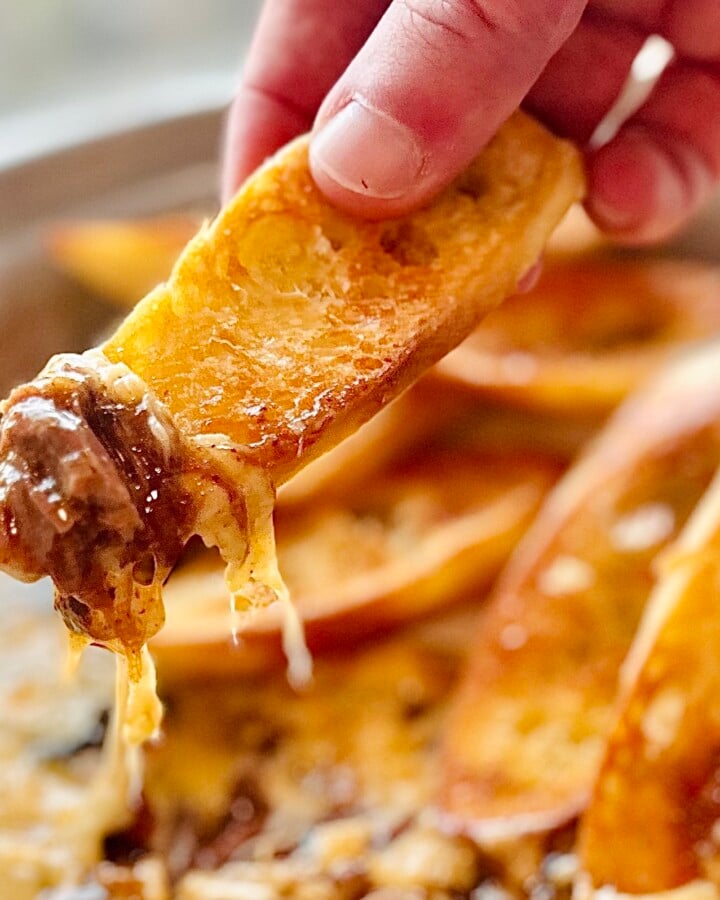 Baguette slice lifted from the pot showing tender beef strands and melted Gruyère stretching.