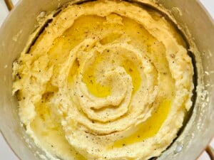 Close-up of fluffy mashed potatoes in a saucepan, topped with melted butter and freshly ground pepper.