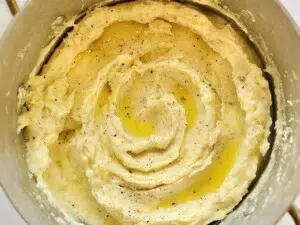 Close-up of fluffy mashed potatoes in a saucepan, topped with melted butter and freshly ground pepper.