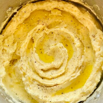 Close-up of fluffy mashed potatoes in a saucepan, topped with melted butter and freshly ground pepper.