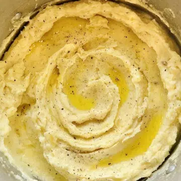 Close-up of fluffy mashed potatoes in a saucepan, topped with melted butter and freshly ground pepper.