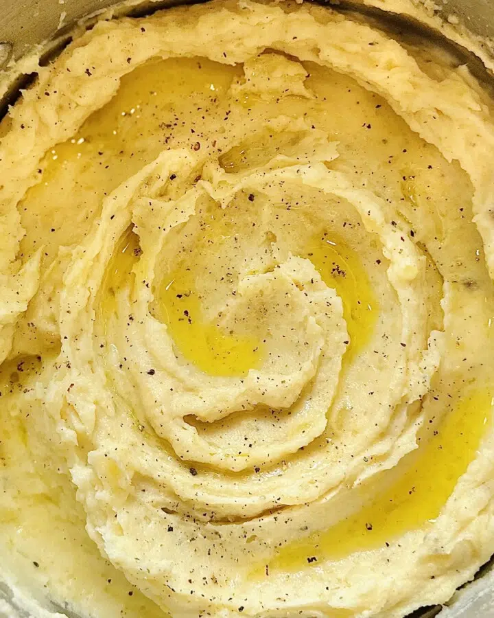 Close-up of fluffy mashed potatoes in a saucepan, topped with melted butter and freshly ground pepper.