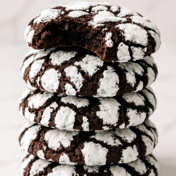 Stacked chocolate crinkle cookies with a bite taken out, revealing fudgy centers and crackly powdered sugar coating