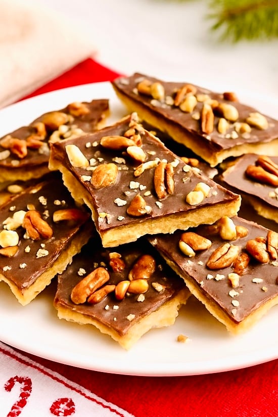 Stacked pieces of saltine cracker toffee bark with a caramel toffee layer, smooth chocolate topping, chopped pecans, and sea salt on a holiday plate.