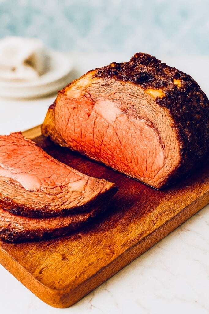 Sliced prime rib roast with herb garlic crust resting on a wooden cutting board