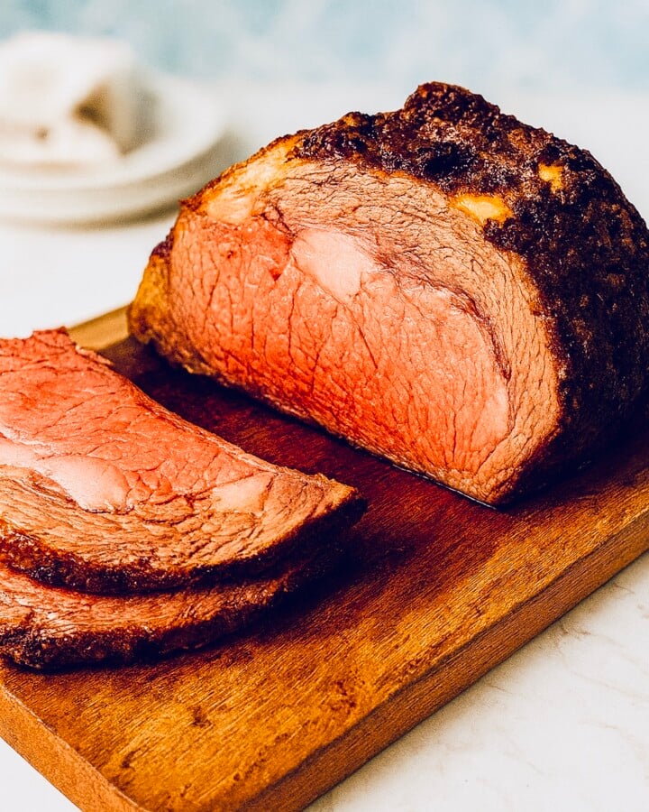 Sliced prime rib roast with herb garlic crust resting on a wooden cutting board