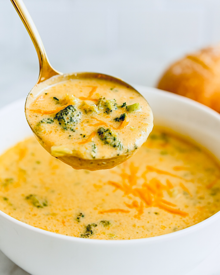 Creamy broccoli cheddar soup ladled from a white bowl, showing a thick, smooth texture with bite-size broccoli pieces and melted cheddar throughout.