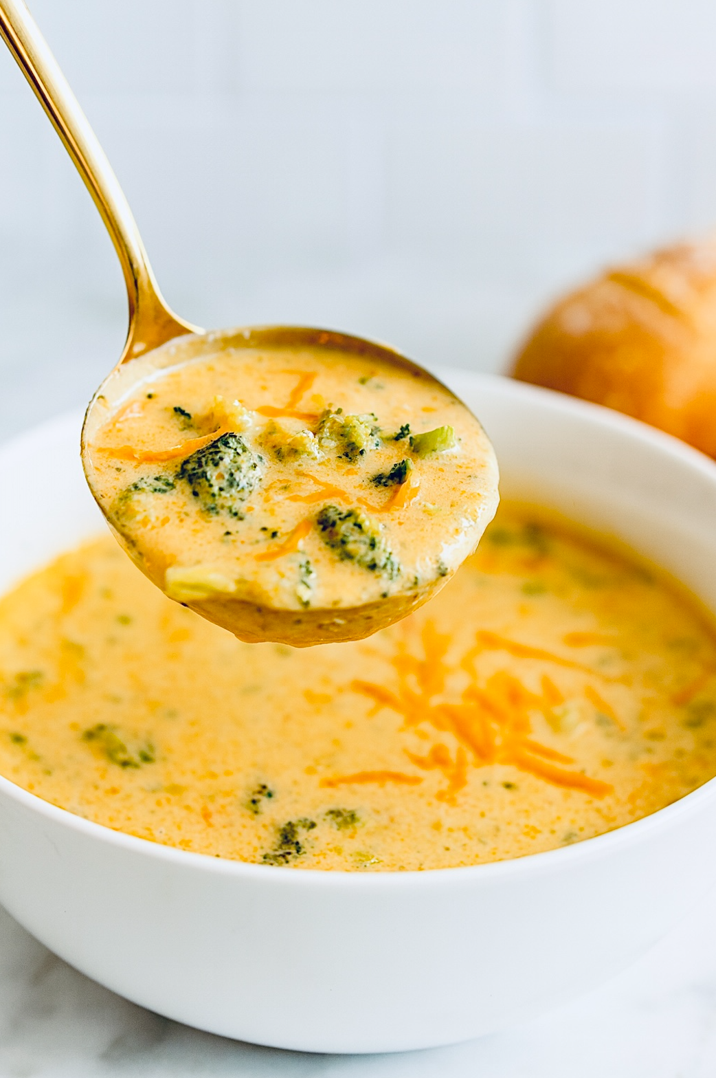 Creamy broccoli cheddar soup ladled from a white bowl, showing a thick, smooth texture with bite-size broccoli pieces and melted cheddar throughout.