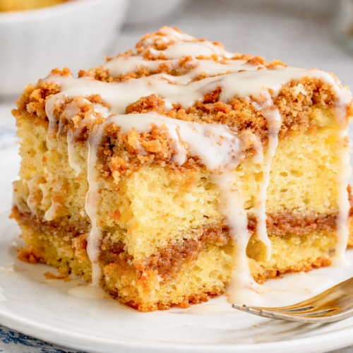 Slice of sour cream coffee cake with cinnamon streusel and vanilla glaze on a white plate