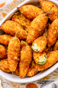 Crispy fried jalapeño poppers with a golden breadcrumb coating and creamy cheese filling in a white serving dish