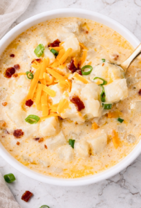Creamy hashbrown potato soup topped with shredded cheddar cheese, bacon bits, and sliced green onions in a white bowl