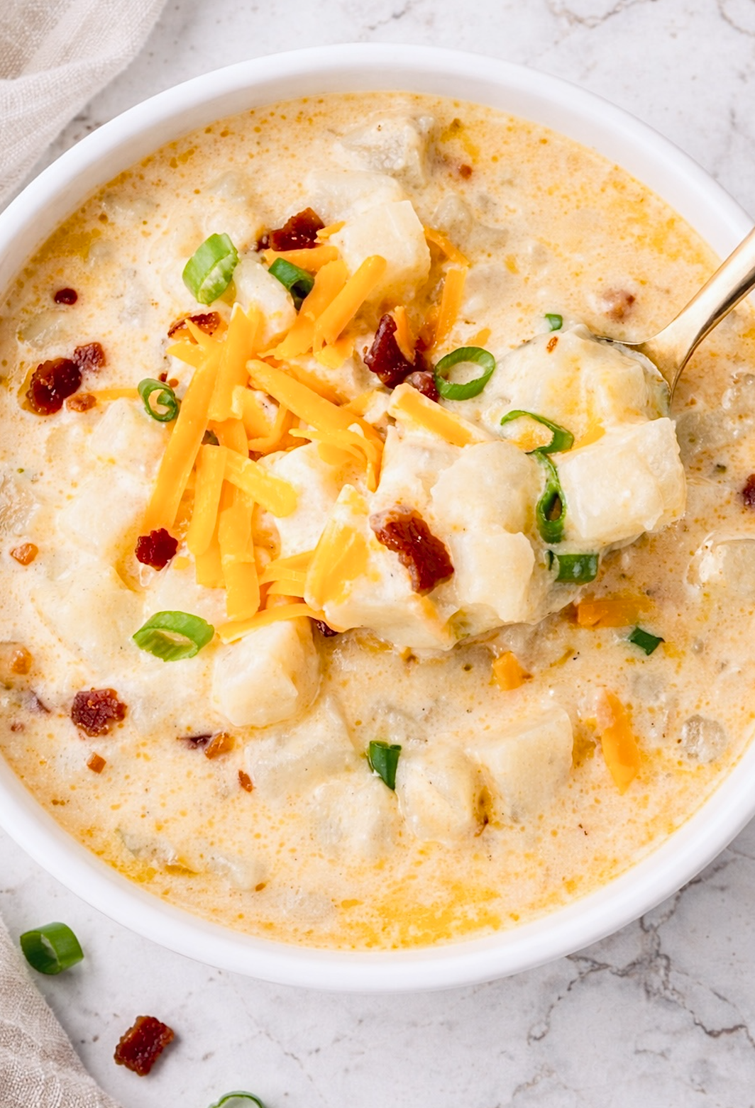 Creamy hashbrown potato soup topped with shredded cheddar cheese, bacon bits, and sliced green onions in a white bowl