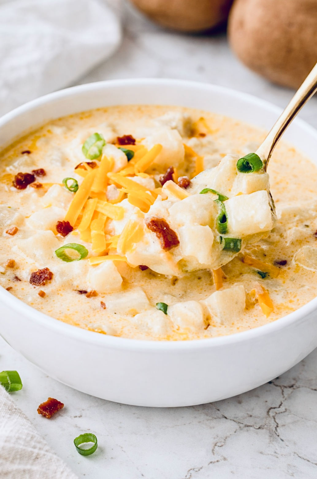Spoon lifting creamy hashbrown potato soup with tender potato cubes, melted cheddar cheese, bacon, and green onions