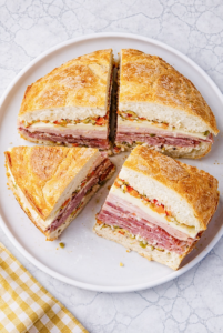 Top-down view of classic New Orleans muffuletta sandwich cut into four wedges on a round white plate, showing layers of Italian meats, cheeses, and olive salad.