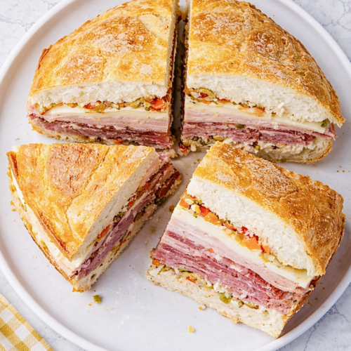 Top-down view of classic New Orleans muffuletta sandwich cut into four wedges on a round white plate, showing layers of Italian meats, cheeses, and olive salad.