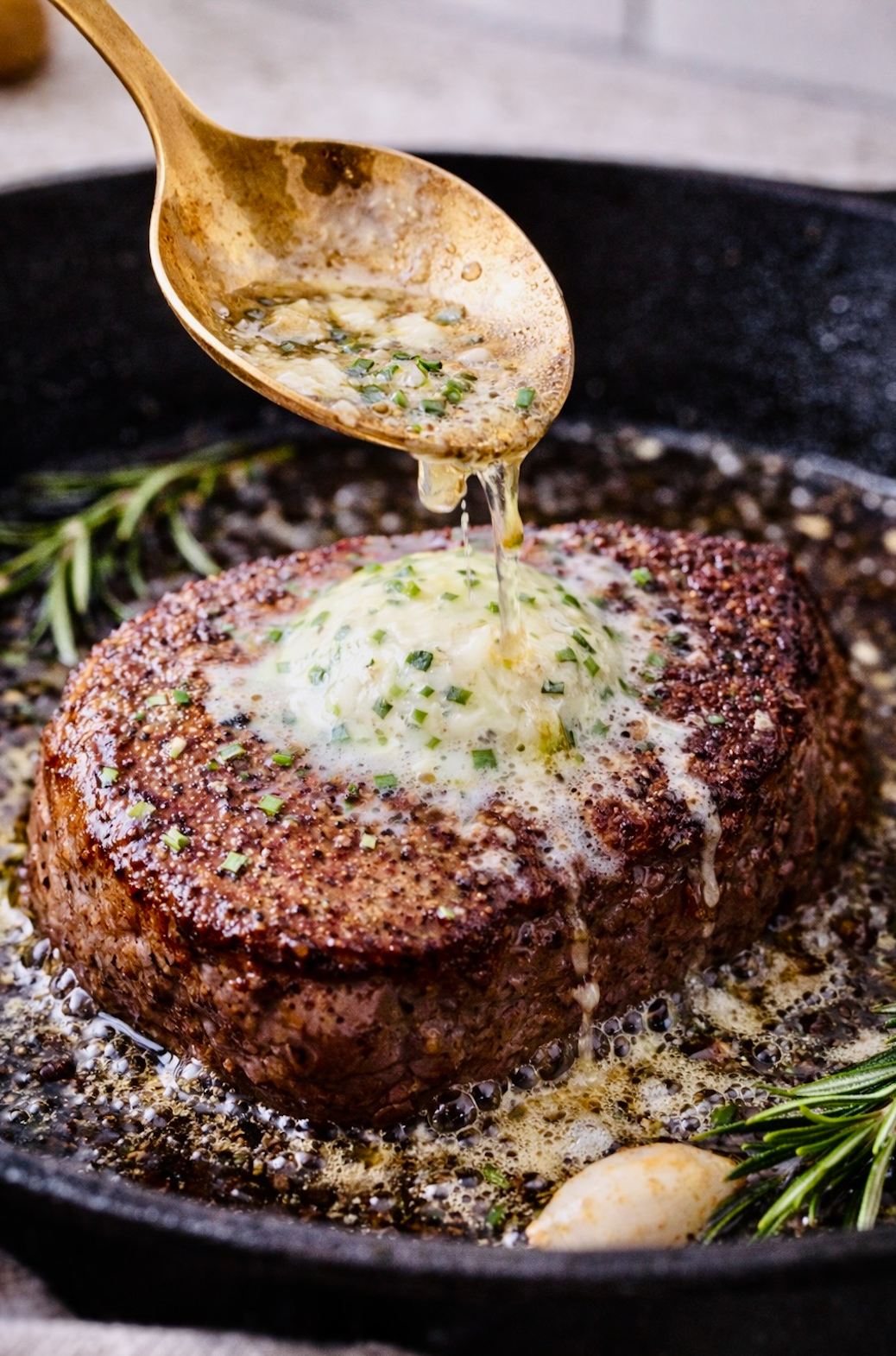Close-up of a thick ribeye steak in a hot cast iron pan as melted garlic herb butter is spooned over the crust, showing sizzling juices and fresh rosemary.