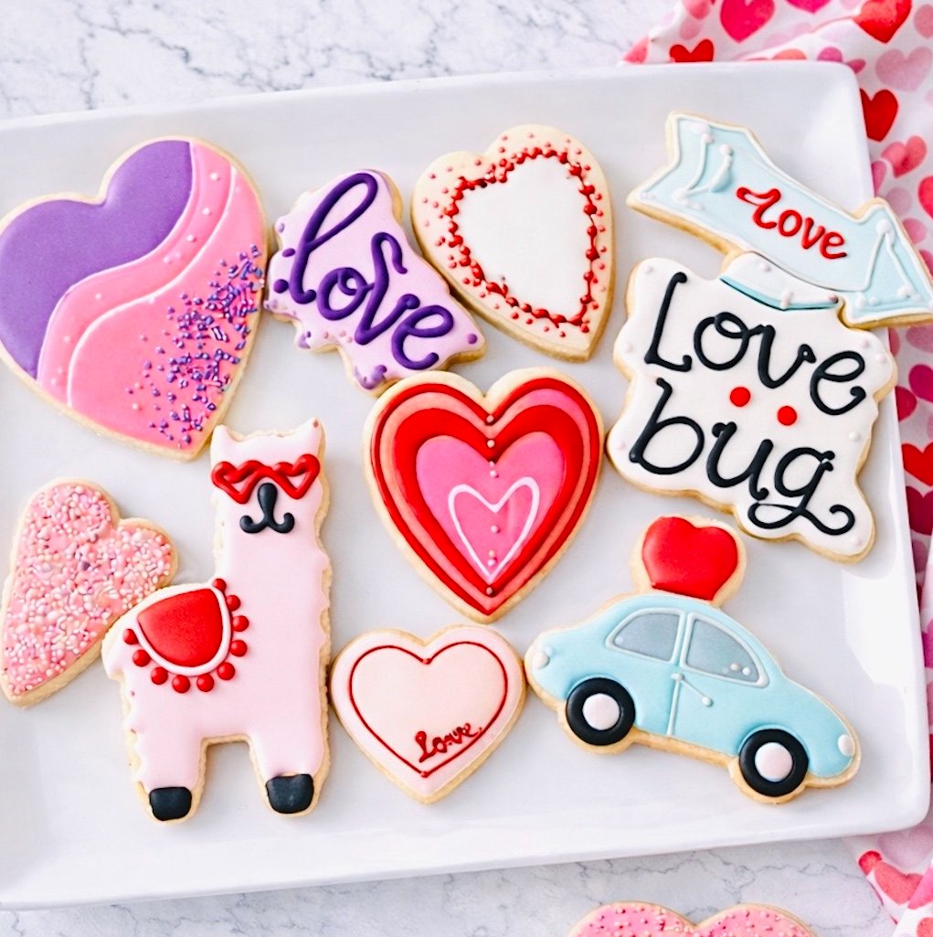 Decorated Valentine's Day sugar cookies on a white plate with heart designs, royal icing details, and pink and red accents on a marble countertop.