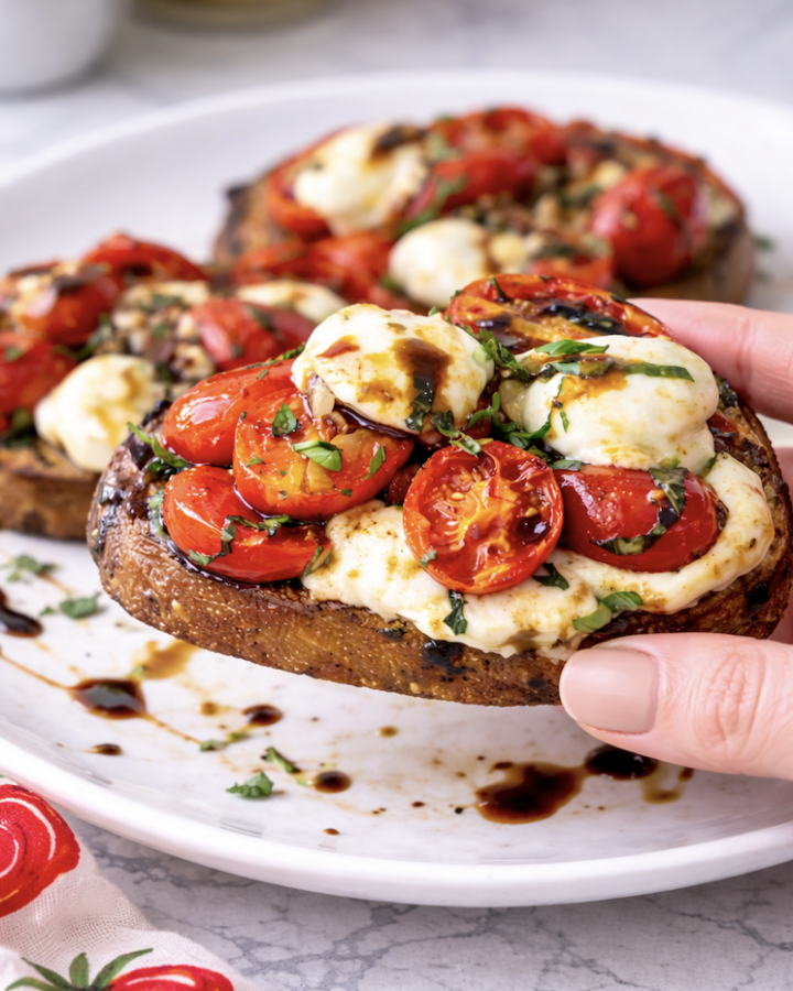 Hand holding tomato bruschetta with mozzarella and balsamic glaze on crispy toasted bread