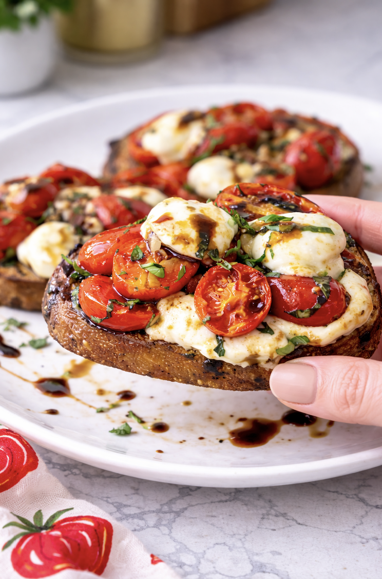 Hand holding tomato bruschetta with mozzarella and balsamic glaze on crispy toasted bread