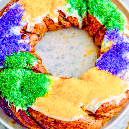 Traditional Mardi Gras king cake with purple, green, and gold sugar on a white plate
