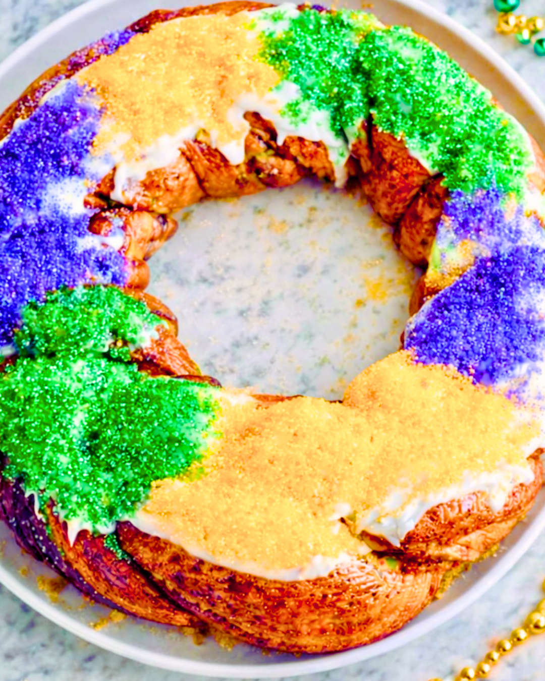 Traditional Mardi Gras king cake with purple, green, and gold sugar on a white plate