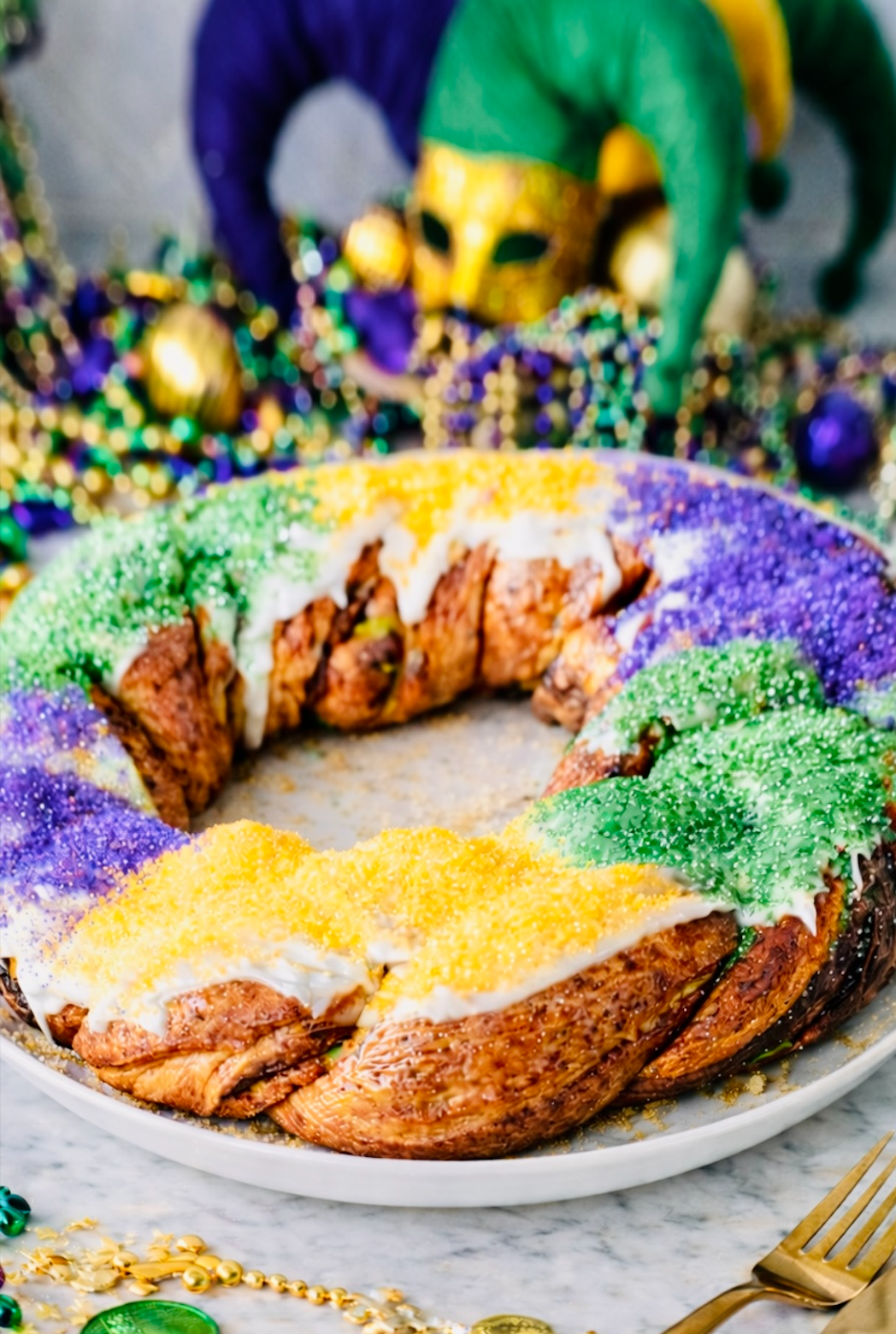 New Orleans–style king cake decorated with Mardi Gras colors and beads in the background