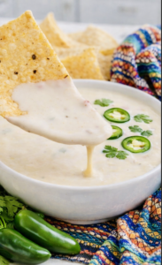 Creamy queso blanco dip in a white bowl garnished with sliced jalapeños and cilantro, served with tortilla chips on a colorful Mexican-style cloth.Creamy queso blanco dip in a white bowl garnished with sliced jalapeños and cilantro, served with tortilla chips on a colorful Mexican-style cloth.