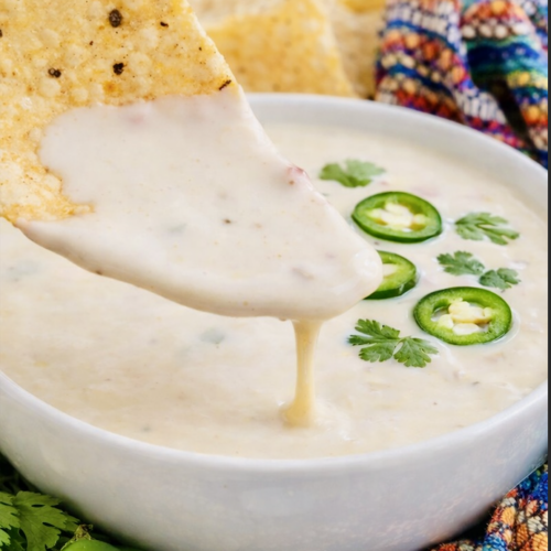 Creamy queso blanco dip in a white bowl garnished with sliced jalapeños and cilantro, served with tortilla chips on a colorful Mexican-style cloth.Creamy queso blanco dip in a white bowl garnished with sliced jalapeños and cilantro, served with tortilla chips on a colorful Mexican-style cloth.