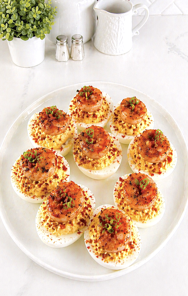 Overhead platter of Cajun shrimp deviled eggs with bacon arranged for serving on white dish in bright kitchen setting