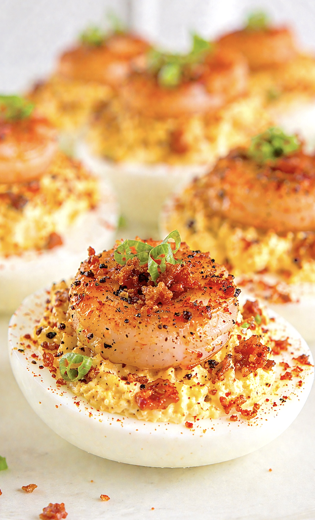 Macro close-up of Cajun shrimp deviled egg with creamy yolk filling, crispy bacon bits, and Cajun seasoning