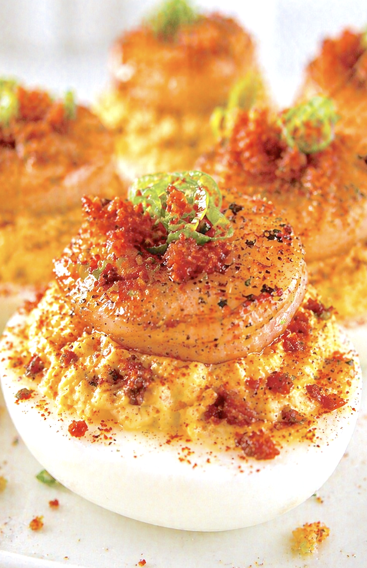 Extreme close-up of Cajun shrimp deviled egg topped with seared shrimp, bacon crumbles, and green onion garnish