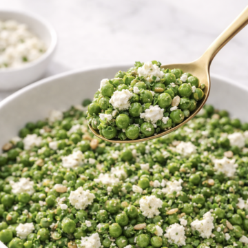 Cropped Spoonful of spring pea salad with feta, mint, chives, and sunflower seeds lifted above a white serving bowl