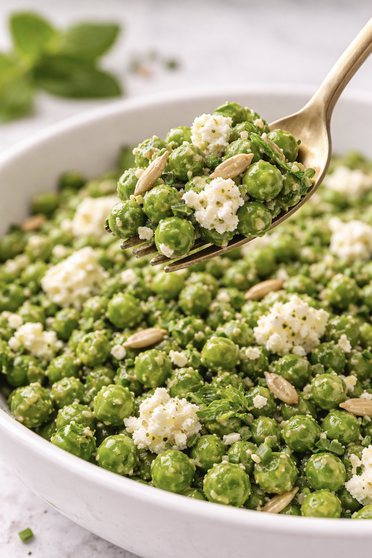 Fork lifting a bite of spring pea salad with feta and sunflower seeds from a white serving bowl