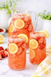 Pitcher and glasses of homemade strawberry lemonade with fresh strawberries and lemon slices over ice.