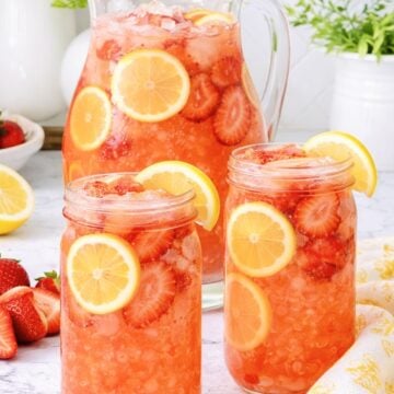 Pitcher and glasses of homemade strawberry lemonade with fresh strawberries and lemon slices over ice.