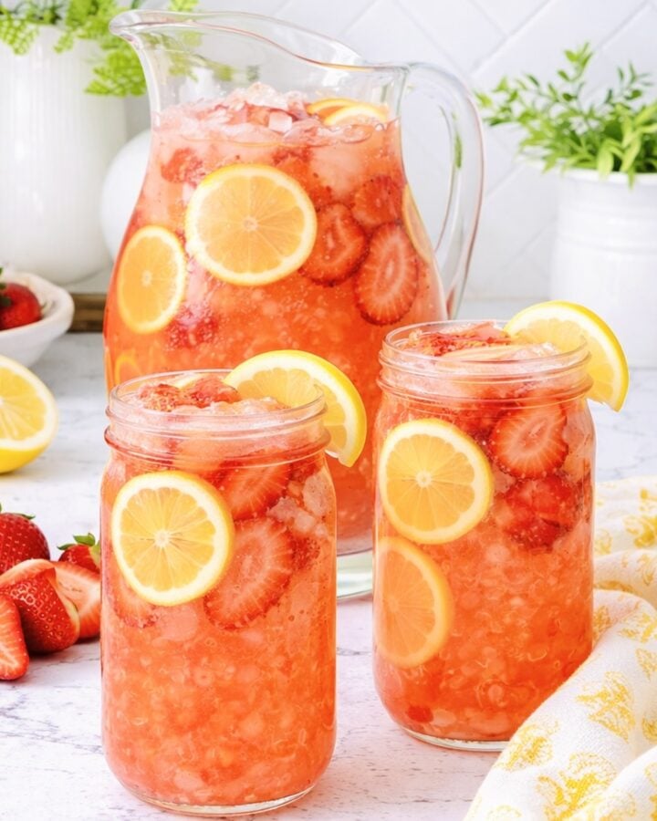 Pitcher and glasses of homemade strawberry lemonade with fresh strawberries and lemon slices over ice.
