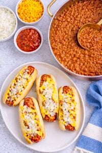 Overhead view of Coney Island hot dogs with chili sauce, mustard, chopped onions, and a pan of sauce