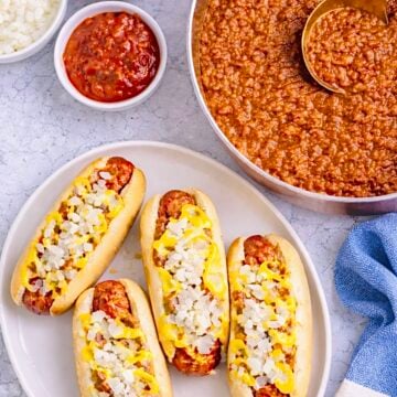 Overhead view of Coney Island hot dogs with chili sauce, mustard, chopped onions, and a pan of sauce