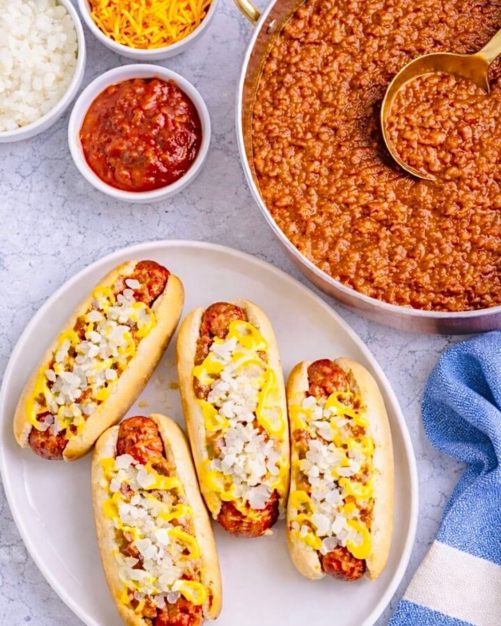 Overhead view of Coney Island hot dogs with chili sauce, mustard, chopped onions, and a pan of sauce